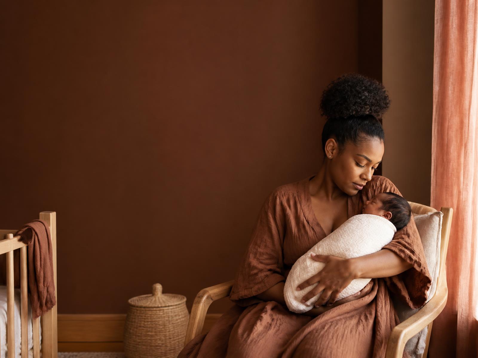 A mother holding her newborn wrapped in a cream swaddle